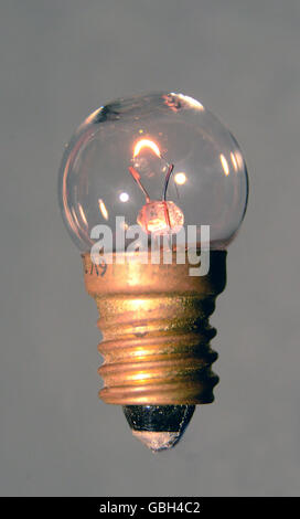 Small Edison light bulb with light seen on a gray background. Stock Photo