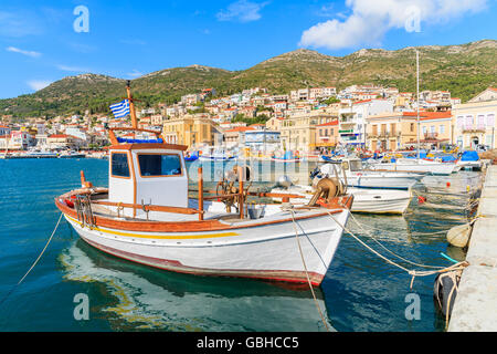 Traditional Greek boat in port of Samos with colourful houses in background, Greece Stock Photo