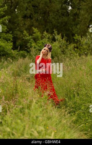 Blonde romantic fairy elf model in meadow with with gold purple rose crown headdress, contemplative, dramatic Stock Photo