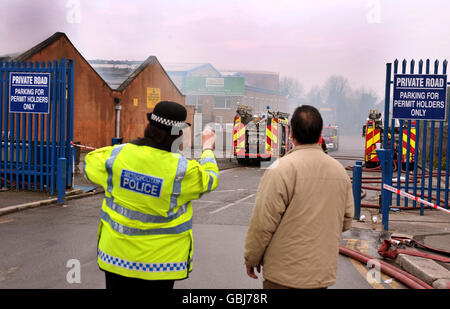 A police officer talks to a member of the public near the scene of a fire at a series of warehouses and office buildings which were destroyed in the huge blaze in Leyton, east London. Stock Photo