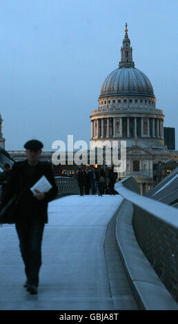 A man walks along the Millennium Bridge at dusk with St Paul's Cathedral visible in the background, London.