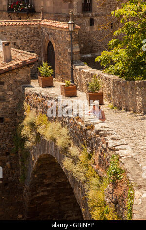 Woman wearing a hat standing on the medieval bridge of San Cayetano over the river Deva in the Spanish town of Potes in the Picos de Europa Spain Stock Photo