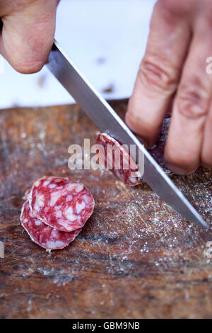 Close up of hands cutting a sausage on a wooden table Stock Photo