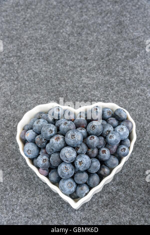 Fresh blueberries in a white heart shaped bowl, on gray background Stock Photo