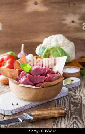 Raw veal cut into pieces with vegetables and other ingredients ready to cook on wooden rustic table, organic cooking concept Stock Photo