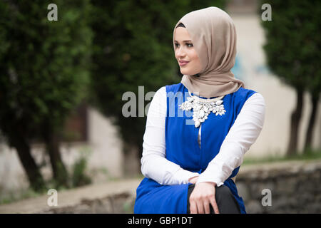 Portrait Of Young Muslim Woman Sitting On Bench In Park Stock Photo