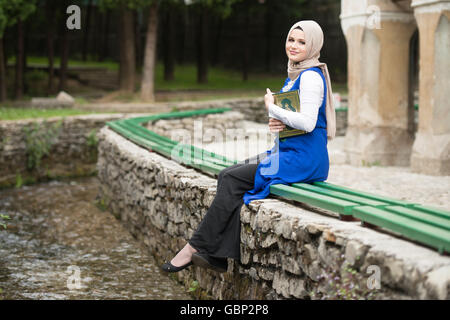 Young Muslim Woman Is Reading The Koran Outdoors Stock Photo