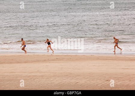 Three middle aged people,two men and one woman,running along the beach in swimming wear Stock Photo