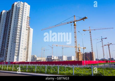 Block of flats under construction, working cranes are under blue sky Stock Photo