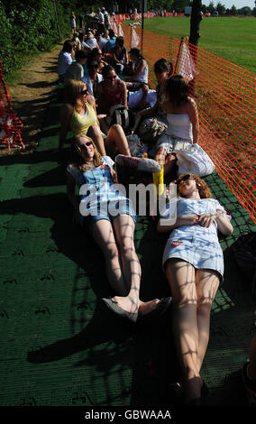 Tennis fans sunbathe in the early morning sun as they queue for the Wimbledon Championships at the All England Lawn Tennis and Croquet Club, Wimbledon, London. Stock Photo