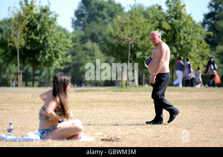 A man looks on as a girl sunbathes in Hyde Park, London. Stock Photo