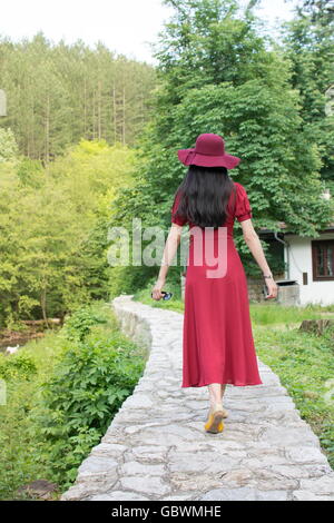 Woman walking the path in park wearing red dress Stock Photo
