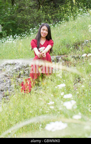 Young woman in flower field wearing red dress Stock Photo