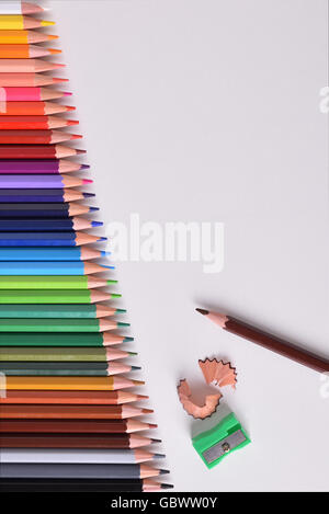 Background colored pencils lined up palette on white table with pencil sharpener. Top view. Vertical composition Stock Photo