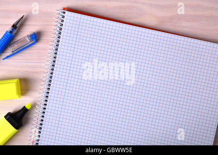 Open notebook checkered to the right of the frame with pen and marker on a wooden table. Top view Stock Photo