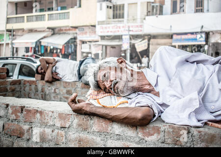 Homeless and tired man in India sleeping on the roadside brickwall in a very hot summer afternoon. Stock Photo