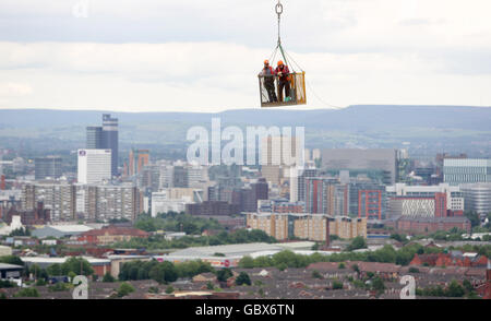 Workmen are lowered in position over the Manchester skyline as work continues on Media City in Salford Quays, Manchester. Stock Photo