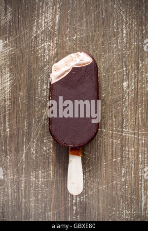 Bitten chocolate covered vanilla ice cream bar on a wooden stick Stock Photo