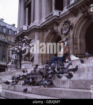 1970s, historical, a man feeding pigeons on the steps of the famous Opera house or Palais Garnier, Paris, France. Stock Photo