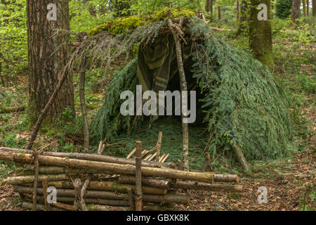 Survival shelter and survivor concept.  A-frame shelter construction shelter with log fire reflector in front of shelter opening Stock Photo