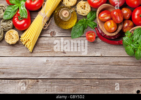 Italian food cooking. Tomatoes, basil, spaghetti pasta, olive oil and chili pepper on wooden kitchen table. Top view with copy s Stock Photo