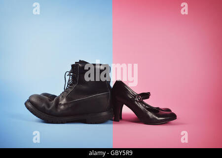 A man's boots and woman's high heels are against a blue and pink isolated background for a struggle or gender power concept. Stock Photo