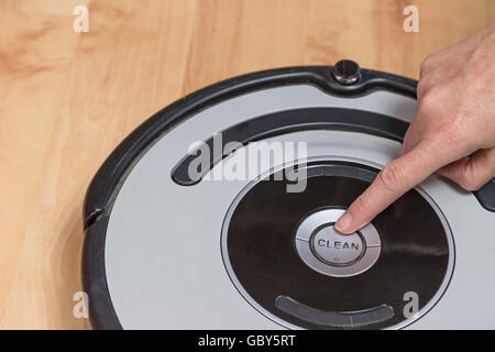 Feminine finger is ready to push button CLEAN on the used robotic vacuum cleaner. All potential trademarks are removed. Stock Photo