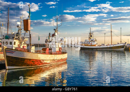 Traditional old wooden fisherman boats lying in the harbor of Husavik in beautiful golden evening light at sunset, Iceland Stock Photo