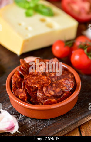 closeup of an earthenware bowl with some slices of Spanish chorizo, a pork sausage typical of Spain, on a rustic wooden table wi Stock Photo