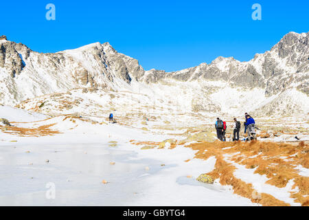 Group of tourists walking along frozen lake in Hincova valley in winter landscape of Tatra Mountains, Slovakia Stock Photo