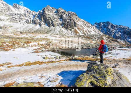 Young woman backpacker tourist standing in Hincova valley and looking at mountains covered with snow, Tatra Mountains, Slovakia Stock Photo