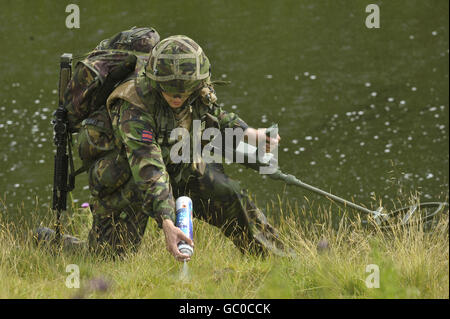 A soldier from the 1st Battalion Royal Welsh, pictured holding an army issue metal detector used to search for Improvised Explosive Devices sprays white floor marking paint on the grass to signify a safe route for following troops, that has been checked and swept for IED's, so soldiers can pass safely during a pre-deployment training exercise, in Brecon, in advance of their mission to Afghanistan in early October. Stock Photo