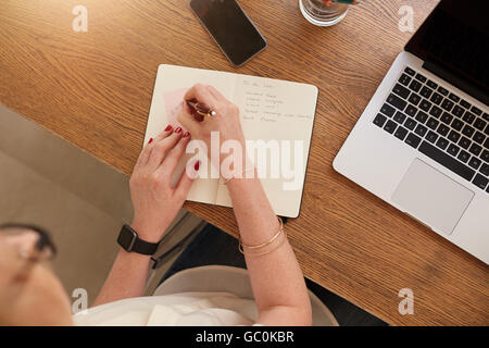 Top view image of woman taking notes with a laptop on table. Woman working at home. Stock Photo
