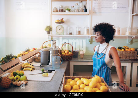 Indoor shot of young female bartender wearing apron standing at juice bar counter looking away and thinking. Stock Photo