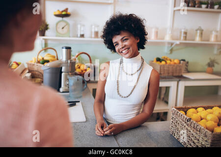 Smiling female waiter receiving order from customer at juice bar. Juice bar owner talking with female customer. Stock Photo