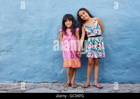 Full length portrait of two little beautiful girls standing together against blue wall. Cute little girls posing together with s Stock Photo
