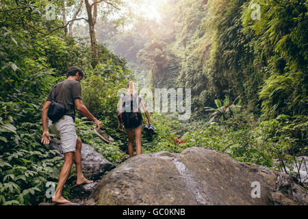 Rear view shot of young couple walking through the forest barefooted. Man and woman hiking on mountain trail. Stock Photo