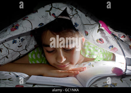 little girl reading a book in bed Stock Photo