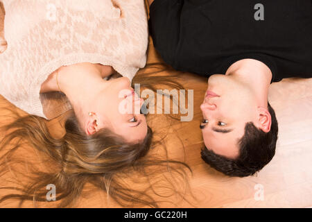 Young couple lying on the floor, man wearing black t-shirt, woman wearing beige blouse, looking in each other's eyes Stock Photo
