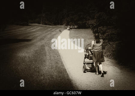 Black and white grainy image in retro style, presenting mother with  pram on walk in the park. View from the back. Stock Photo