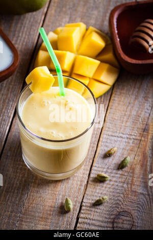 Glass of mango lassi Indian drink flavored with cardamom. Milkshake on wooden background. Stock Photo