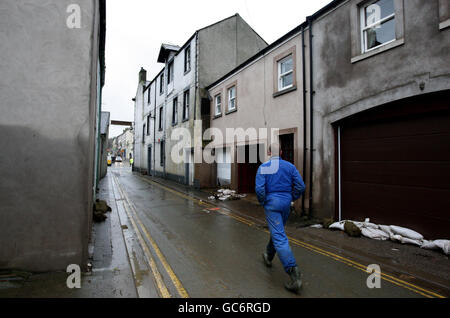 A man walks past a house (left), which is marked by the height of flood water, in a side street in Cockermouth town centre following the recent floods. Stock Photo