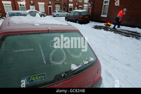 A postman delivers his mail as the overnight temperature is written in ice on a car in Stockport as the arctic conditions continue to hit the north of England. Stock Photo