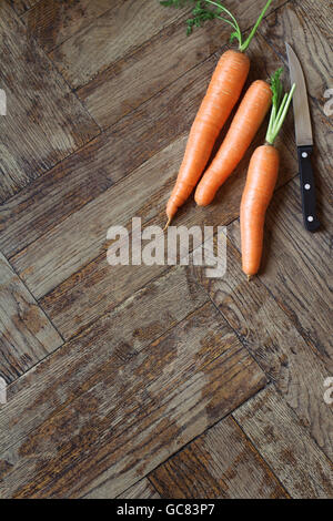 vertical top view of three carrots next to a knife on wooden background Stock Photo