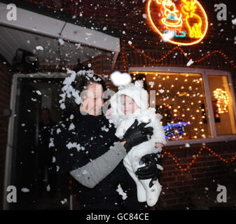 A quiet seaside cul-de-sac has become something of a Christmas attraction as neighbours try to out-do each other with their festive lights. Emily George from Bournemouth holds her 10-week-old neice Molly Carr under a fake snow machine during a visit to the garden of one of the houses in Runton Road, Branksome. Stock Photo