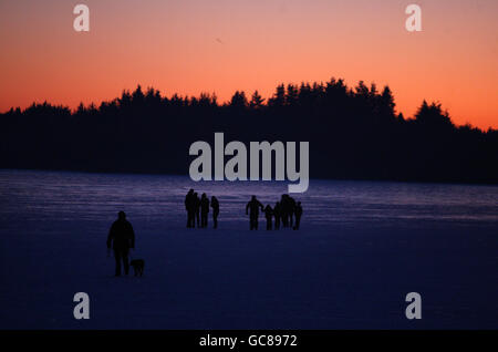 People walk across the frozen Lake of Menteith, to the Inchmahome island at sunset, as temperatures continued to fall throughout Britain. Stock Photo