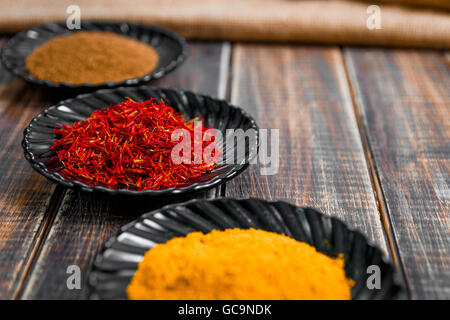 Spices in black ceramic plates on wooden background. Various spices selection, closeup. Saffron, turmeric, curry Stock Photo