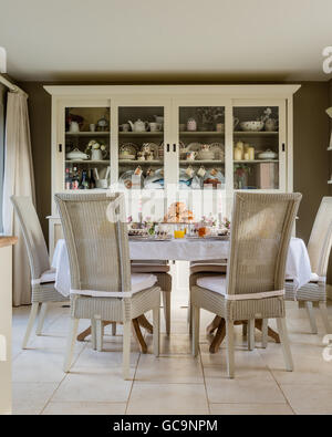 Fulham Lloyd Loom dining chairs around table laid with croissant. A large white dresser stands in the background Stock Photo