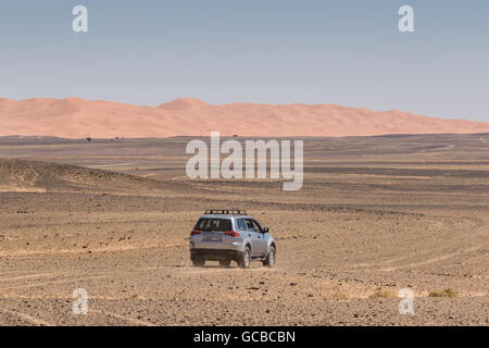 Silver Range Rover traveling into the Morocco desert, heading away from the camera towards sand dunes, blue sky background, Stock Photo