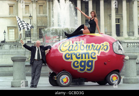 Motor racing commentator Murray Walker gets the Cadbury Creme Eggs 2,000 mile round-the-country creme egg run underway in London. Sitting atop the egg is 'Don't Forget Your Toothbrush' hostess, Jadene Doran. Stock Photo